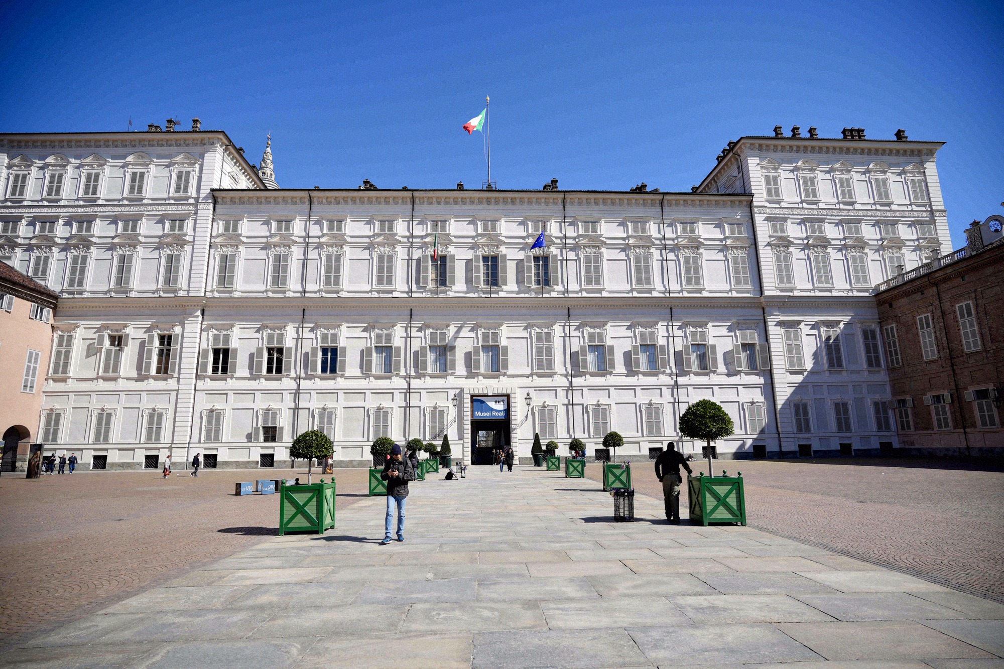 Frontfassade des Palazzo Reale am Piazza Castello mit italienischer und EU-Flagge bei strahlendem Sonnenschein.